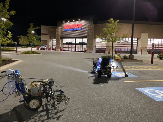 Costco storefront at night, featuring illuminated signage and accessible parking spaces in the foreground.