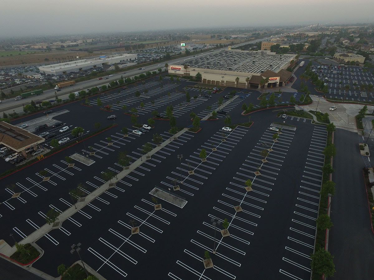 Parking lot of a Costco location with yellow exit sign, marked lanes, and trucks visible in the background under a clear blue sky.
